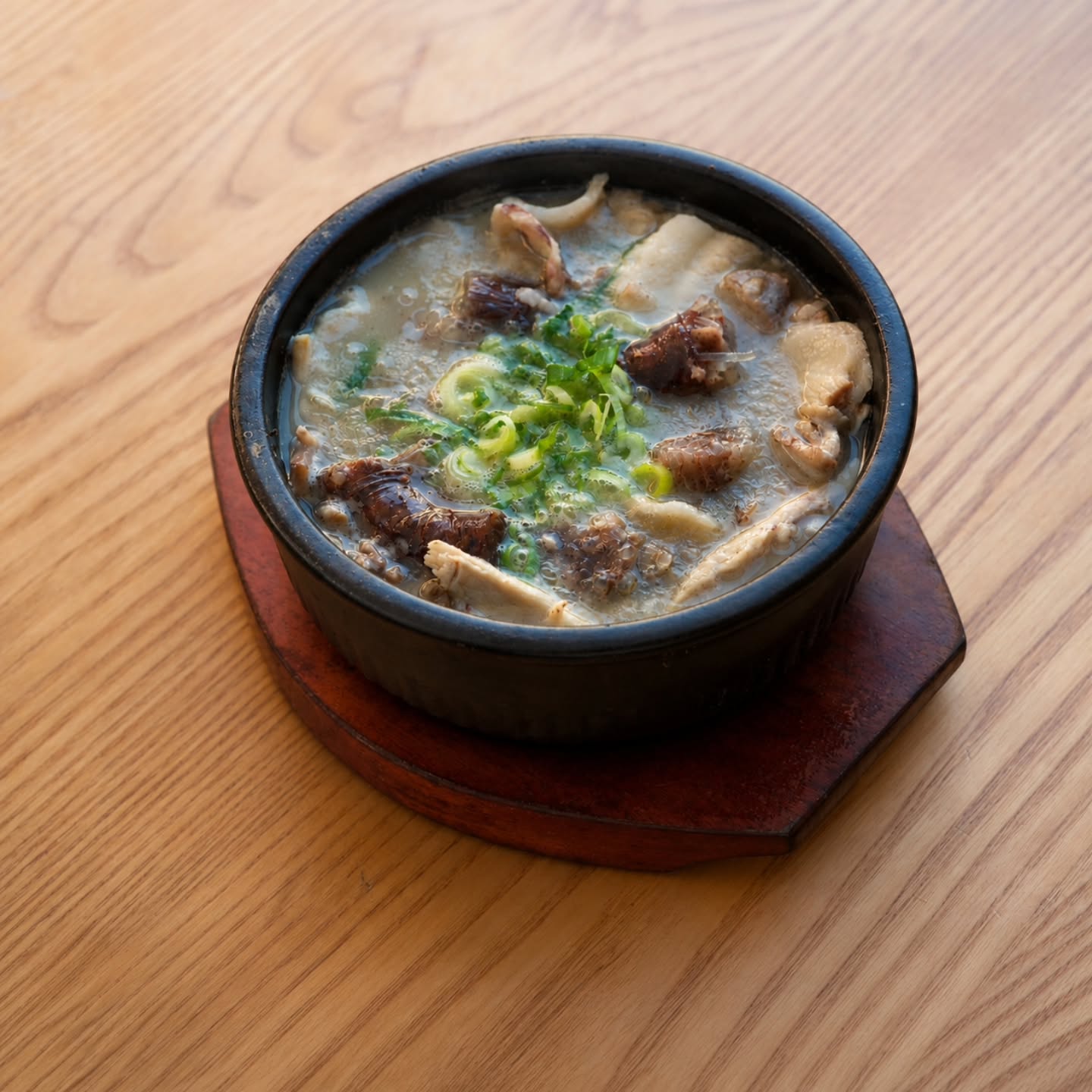 A dark stone bowl of soondaeguk, garnished with spring onion, on a dark wood table